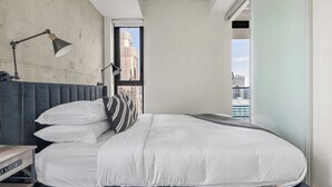 Une chambre moderne avec un grand lit, deux lampes de chevet, une vue sur la ville par une fenêtre et un mur en béton.
