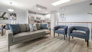 A modern living room with a grey sofa, two blue armchairs, and a wooden dining table. - 3-Bedroom Upper Unit Near Bow River with Yard (Calgary)