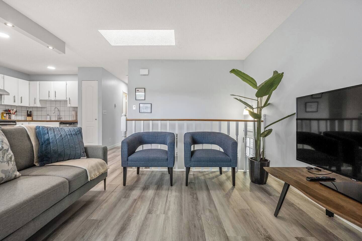 Una sala moderna con un sofá, dos sillones, una mesa de centro, un televisor y una planta grande.
