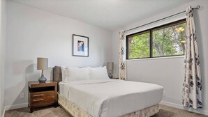 A bedroom with a bed, nightstand, lamp, and a window with curtains. - 3-Bedroom Upper Unit Near Bow River with Yard (Calgary)