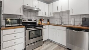 A modern kitchen with white cabinets, stainless steel appliances, and a wooden countertop. - 3-Bedroom Upper Unit Near Bow River with Yard (Calgary)