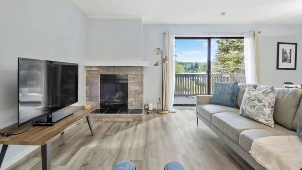 A modern living room with a flat-screen TV, a fireplace, a sofa, and a balcony with a view. - 3-Bedroom Upper Unit Near Bow River with Yard (Calgary)