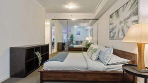 A bedroom with a bed, a bedside table with a lamp, a mirror, and a bookshelf. - A Modern Studio for 6 Next to Darling Harbour (Sydney)