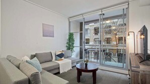 A modern living room with a grey sofa, a small round table, and a large sliding glass door leading to an outdoor balcony. - A Modern Studio for 6 Next to Darling Harbour (Sydney)