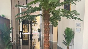 Ένας χώρος υποδοχής με ένα ψηλό φοινικόδεντρο σε μαύκη γλάστρα, γυαλιστερό μάρμαρο στο δάπεδο και μοντέρνο εσωτερικό σχεδιασμό.