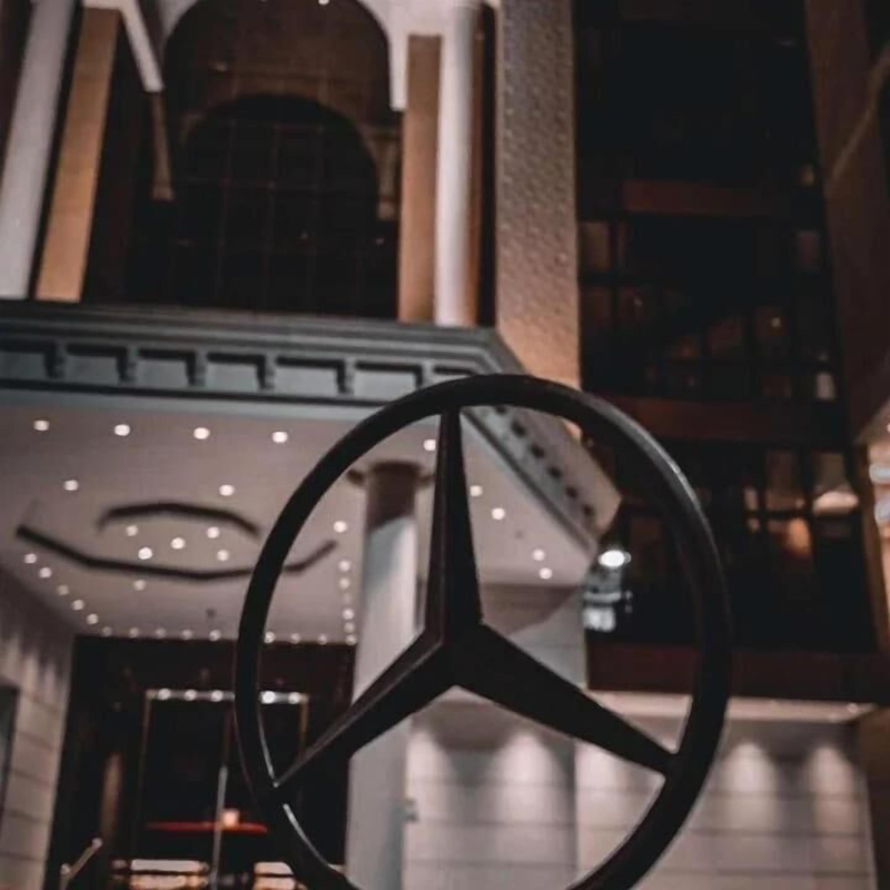 A large, modern building with a prominent Mercedes-Benz logo in the foreground.