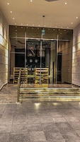 A modern hotel lobby with a glass entrance, a staircase, and a reception desk.