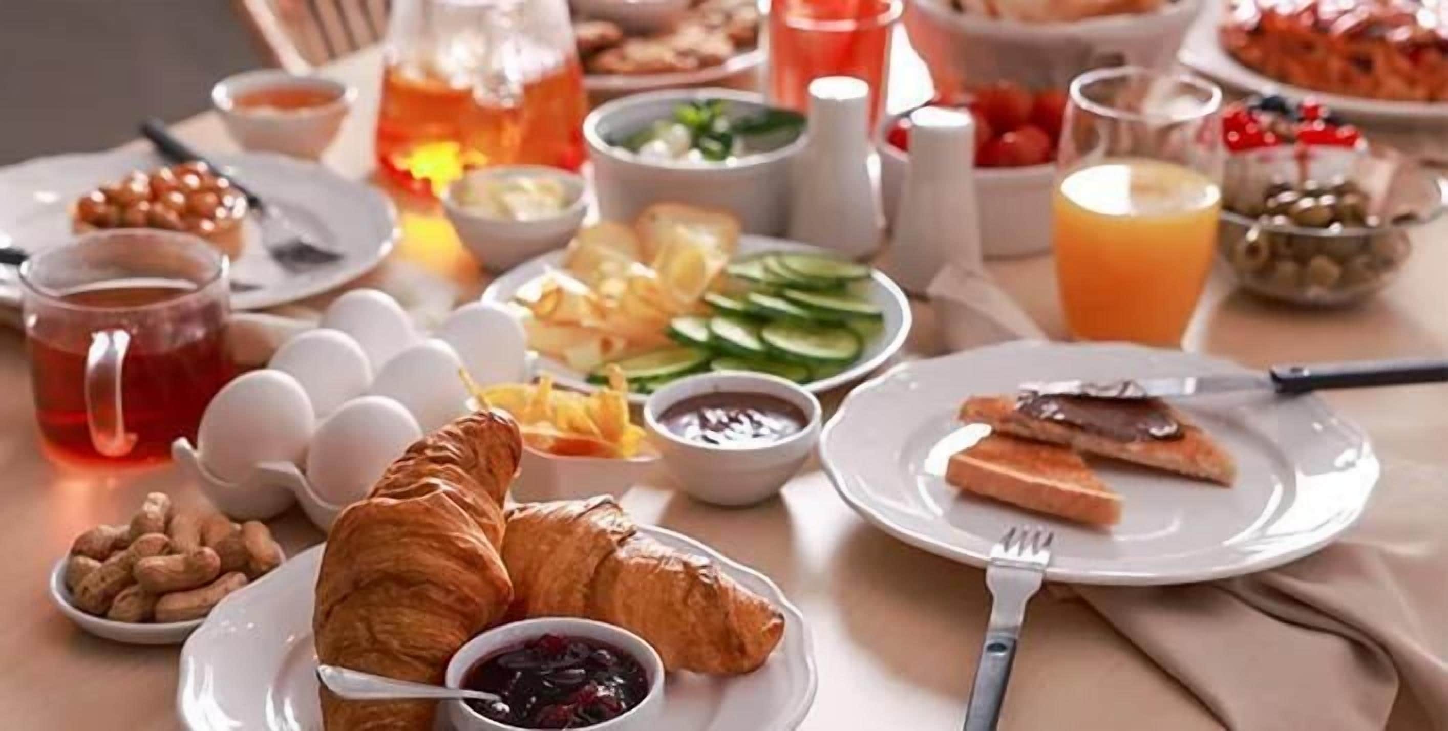 Un desayuno con croissants, huevos, tostadas, fruta y bebidas.