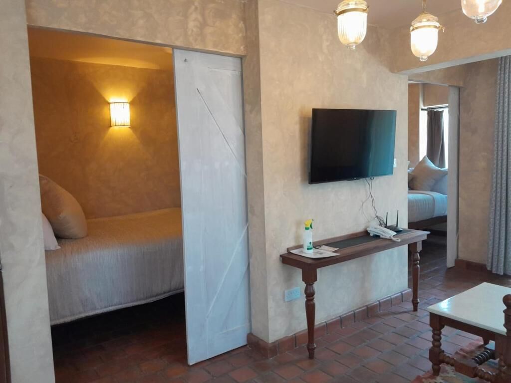 Habitación de hotel con cama, televisor montado en la pared, mesita de noche y ventana con cortinas.