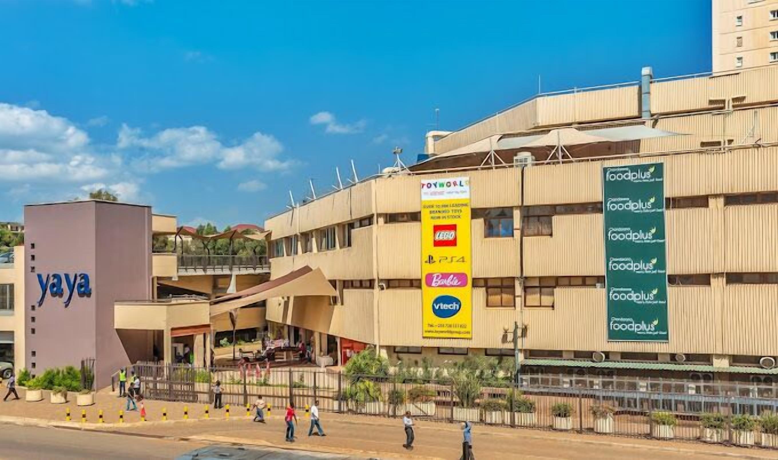 A modern building with a 'yaya' sign, multiple floors, and a 'foodplus' sign advertising various food brands.