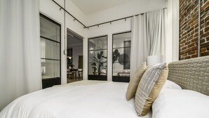 Un dormitorio con una cama grande, una pared de ladrillo y una puerta corrediza de vidrio que da a un comedor.