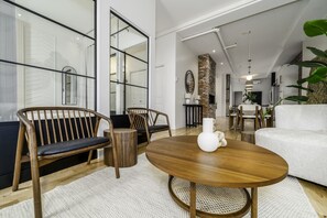 Un salon moderne avec un canapé, des fauteuils, une table ronde en bois et une cheminée en briques.