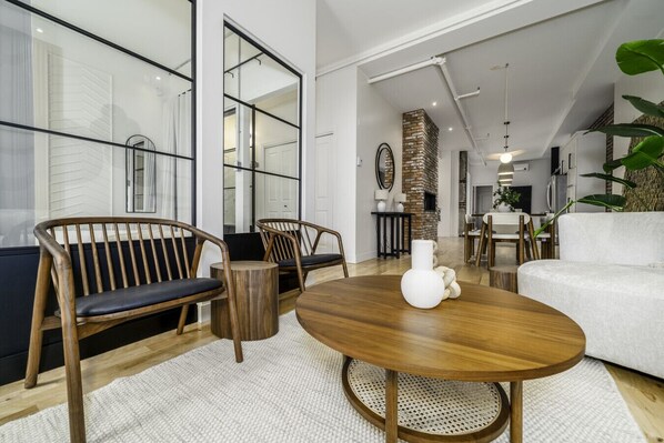 A modern living room with a sofa, chairs, a round wooden table, and a brick fireplace.