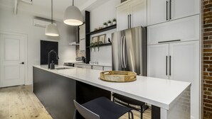 Una cocina moderna con armarios blancos, un refrigerador de acero inoxidable, luces colgantes y una tabla de cortar de madera en la isla.