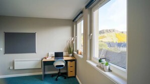 Ein kleiner, ordentlicher Raum mit Schreibtisch, Stuhl und Fenster mit Blick auf eine Hügelkuppe.