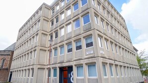 Ein mehrstöckiges Gebäude mit Hauseingang an einer Ecke, großen Fenstern und einem Schild mit der Aufschrift 'Roxburgh Place'.