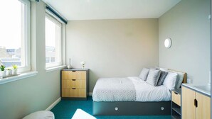 Ein Schlafzimmer mit einem Bett, Nachttischen, einem Fenster und Blick auf Gebäude.
