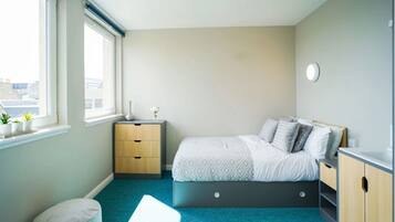 A bedroom with a bed, bedside tables, a window, and a view of buildings outside.