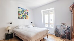 Une chambre à coucher avec un lit, une fenêtre, un tableau et une table de chevet.