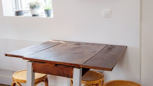 Une pièce avec une table en bois et deux chaises, une fenêtre donnant sur un paysage agréable et une œuvre d’art encadrée accrochée au mur.