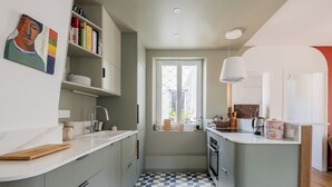 Une cuisine moderne avec des meubles gris, un carrelage à motifs, une fenêtre offrant une belle vue et une bibliothèque remplie de livres et d’objets décoratifs.