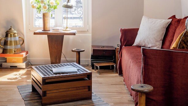Un salon chaleureux avec un canapé rouge, une table basse en bois, une plante en pot et une grande fenêtre laissant entrer la lumière naturelle.