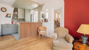 Un salon avec un plancher en bois, un fauteuil en osier, un canapé, une lampe et un mur rouge.