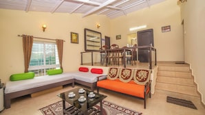 A living room with a sofa, a coffee table, a staircase, and a dining area. - The springs Nilgiris (Kotagiri)