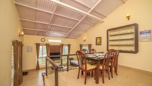 A dining area with a high ceiling, a clock, and a wall-mounted shelf with glasses. - The springs Nilgiris (Kotagiri)