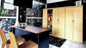 Una pequeña cocina americana con una mesa de madera, sillas de mimbre y un armario con estantes.