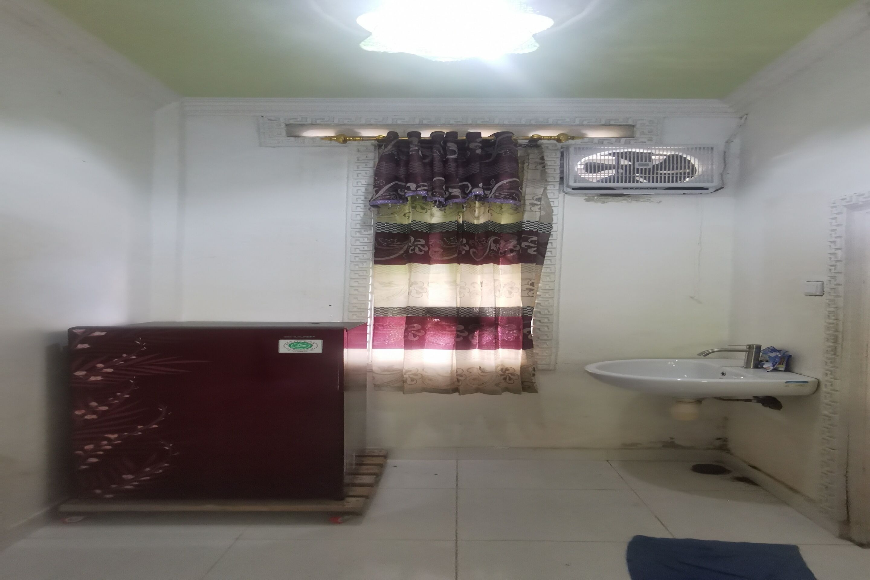A small bathroom with a white sink, a fan, a patterned curtain, and a dark-colored cabinet.