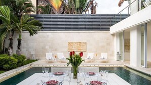 Un espacio exterior para comer con piscina, mesa y sillas blancas, y tulipanes rojos en un entorno moderno.