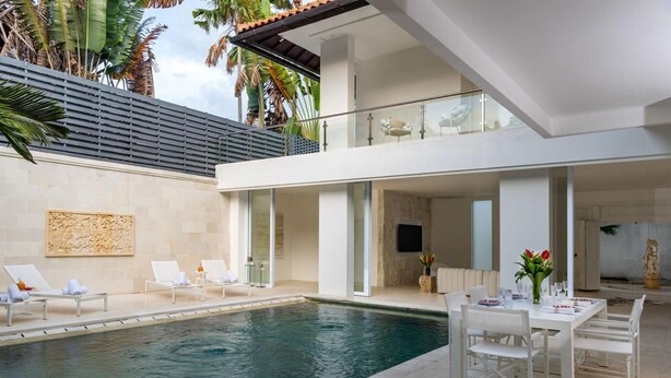 Un área moderna junto a la piscina con sillones de descanso, una mesa de comedor y una vista despejada del agua.