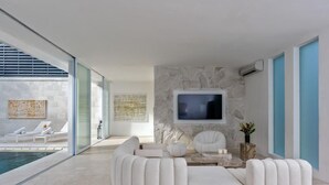 Una sala de estar moderna con una pared de piedra, un televisor de pantalla plana y un área junto a la piscina con sillas de descanso.