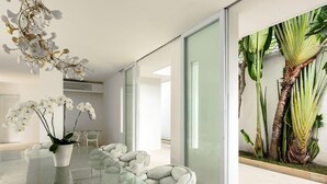 Un interior moderno con una mesa de comedor de vidrio, sillas blancas acolchadas y orquídeas blancas en una maceta blanca.