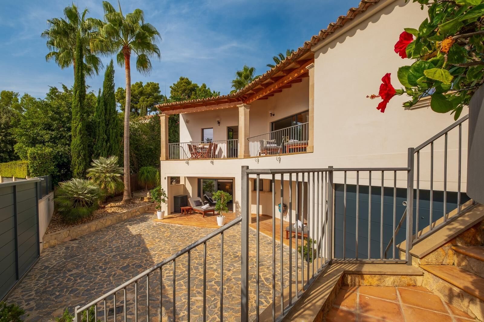 A two-story house with a balcony, a stone patio, and a swimming pool.