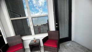 Ein kleiner Balkon mit zwei Korbstühlen und einem Tisch.