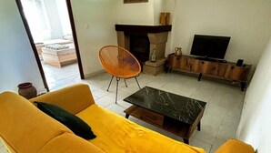 Un salon avec un canapé jaune, une table basse noire, un meuble TV en bois et une cheminée.