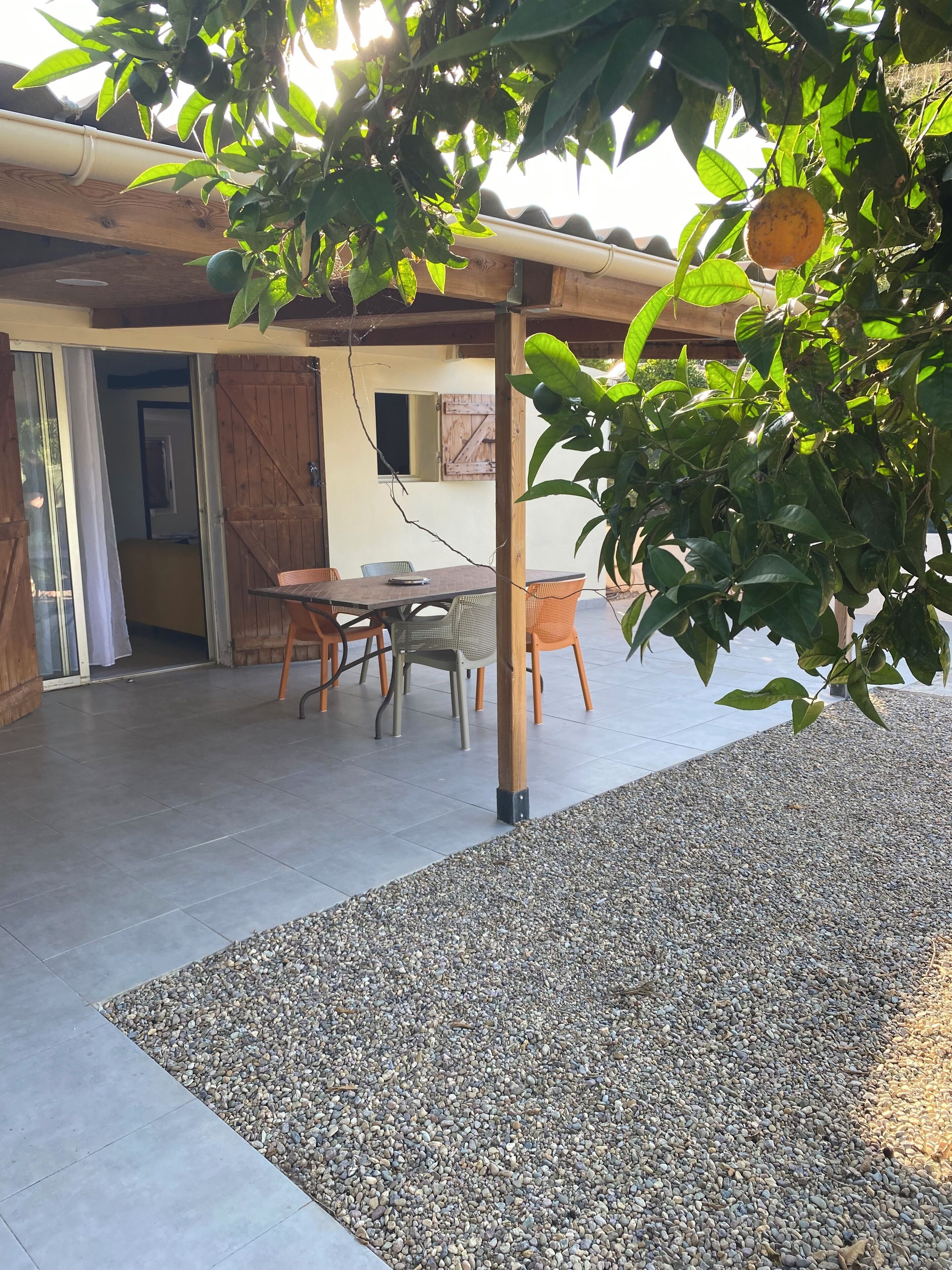 Een terras buiten met een tafel en stoelen, omringd door een grindpad en een houten pergola.