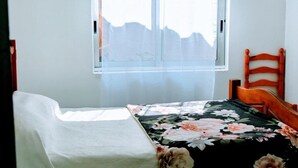 Une chambre à coucher avec un lit, une chaise, une fenêtre avec des rideaux et une tête de lit en bois.