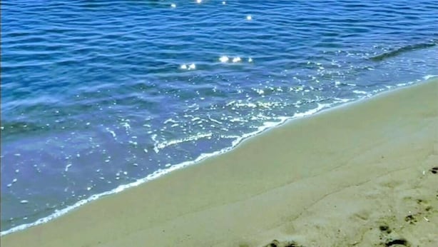 Une plage avec une eau d’un bleu limpide et un soleil éclatant dans le ciel.