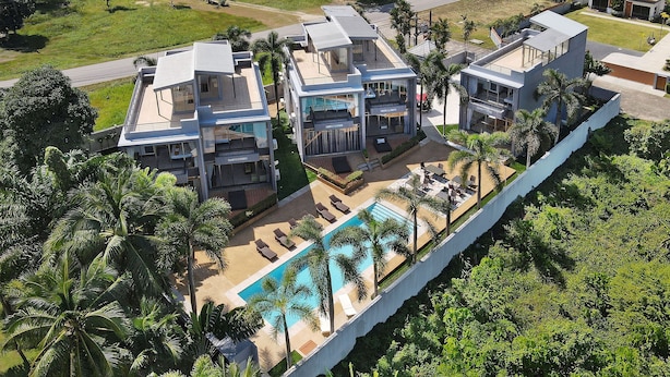 A modern hotel with a pool, surrounded by palm trees and greenery.
