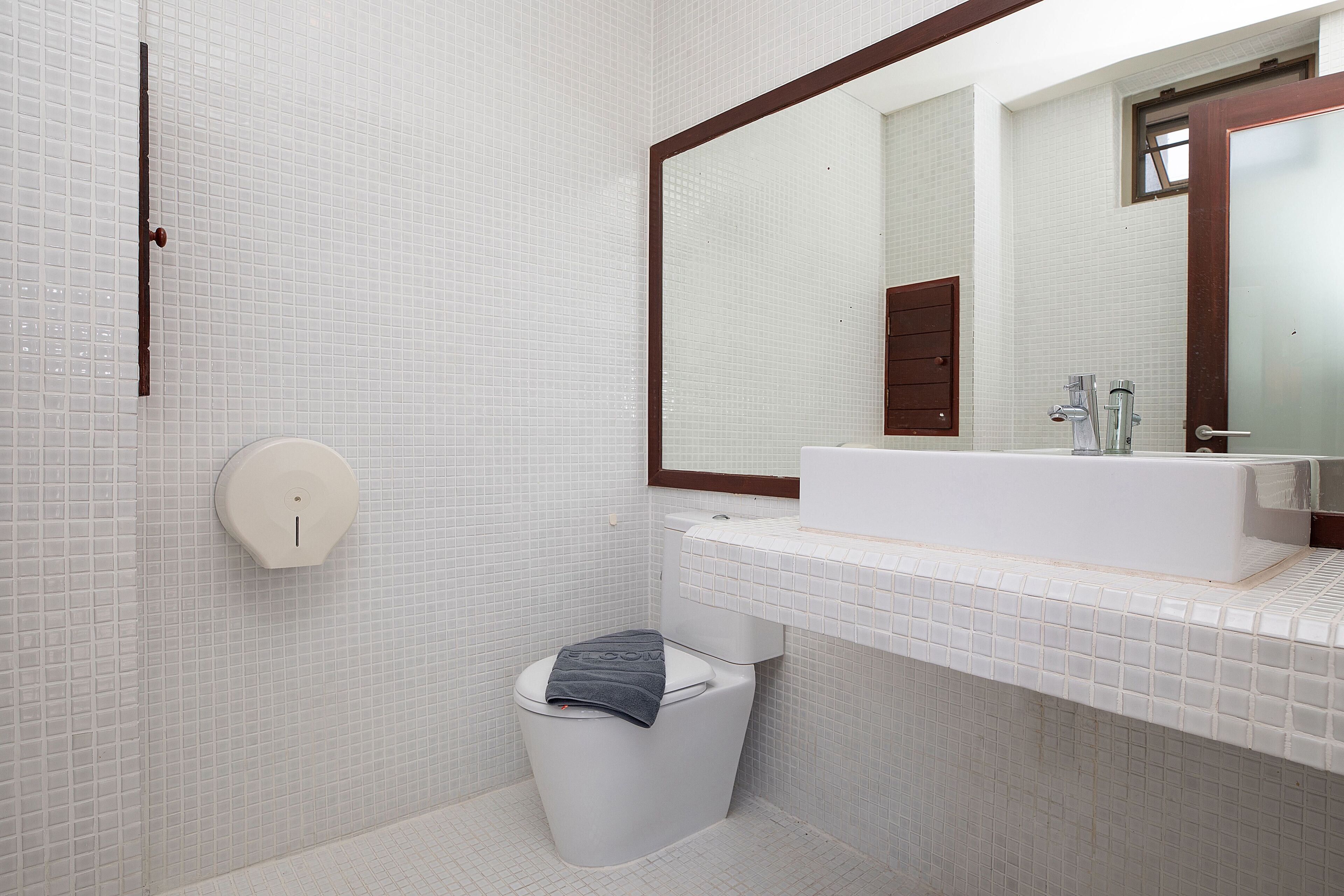 A modern bathroom with a white tiled wall, a large mirror, a white sink, and a toilet.