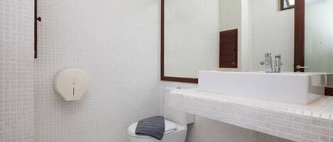 A modern bathroom with a white tiled wall, a large mirror, a white sink, and a toilet.