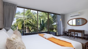 A hotel room with a large bed, a desk, and a view of palm trees through large windows.