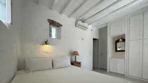 A bedroom with a large bed, a nightstand with a lamp, a wall-mounted light, and a wardrobe with multiple doors. - Stone Built Villa Ferretti #Unoblu (Mykonos)