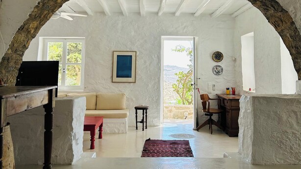A spacious room with a high ceiling, a stone archway, a wooden table, a sofa, and a view through a doorway to an outdoor area. - Stone Built Villa Ferretti #Unoblu (Mykonos)
