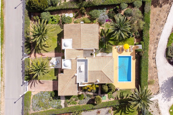 Vue aérienne d’une maison avec un toit en tuiles, une piscine et une végétation luxuriante tout autour.
