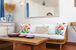 Une pièce avec un canapé blanc, deux coussins colorés, une table en bois sur laquelle sont posés des bols, un vase bleu et un miroir accroché au mur.