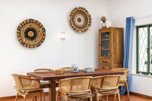 Un coin repas avec une table en bois et des chaises en osier, un meuble avec des portes en verre et des œuvres d’art décoratives accrochées au mur.